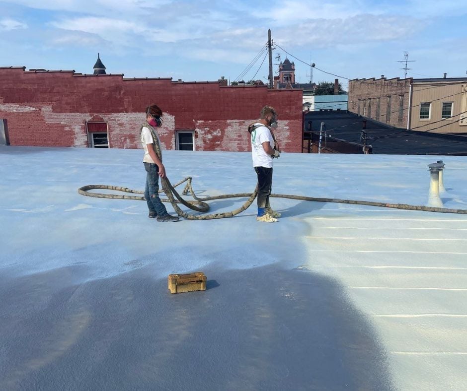 Guy on the right is spraying foam;. Guy on the left is carrying the hoses for the spray foam gun.